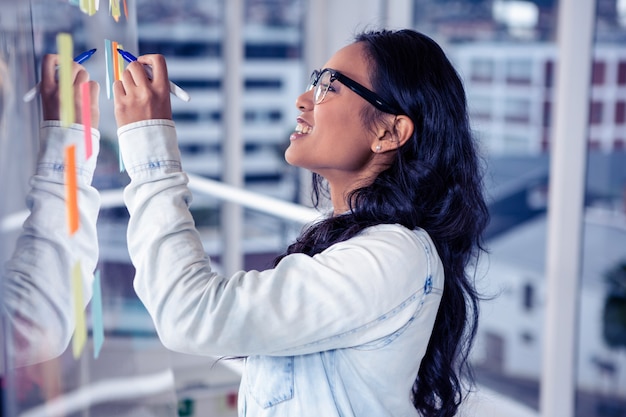 Asian woman writing on sticky notes on glass wall