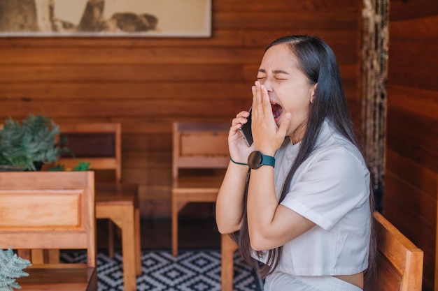 オフィスで電話をしながらあくびをするアジア人女性。