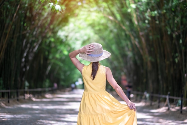 Photo asian woman in yellow dress and hat traveling at green bamboo tunnel happy traveler walking chulabhorn wanaram temple landmark and popular for tourists attractions in nakhon nayok thailand