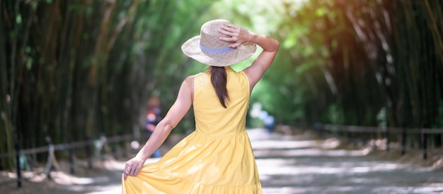 노란 드레스와 모자를 쓴 아시아 여성 녹색 대나무 터널에서 여행하는 행복한 여행자 출랍혼 와나람 사원 랜드마크를 걷고 있으며 태국 나콘나욕의 관광 명소로 유명합니다.