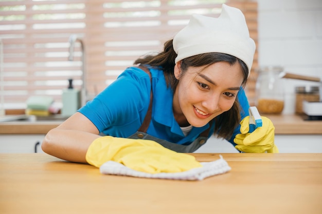노란 장갑을 입은 아시아 여성이 집안 청소를 수행합니다. 액체 스프레이로 부 카운터를 청소합니다. 집의 청결과 위생을 강조합니다.