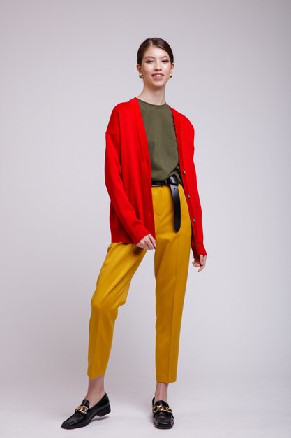 白い背景の上の黄色いズボン赤いカーディガン緑のTシャツベルトのアジアの女性スタジオショット