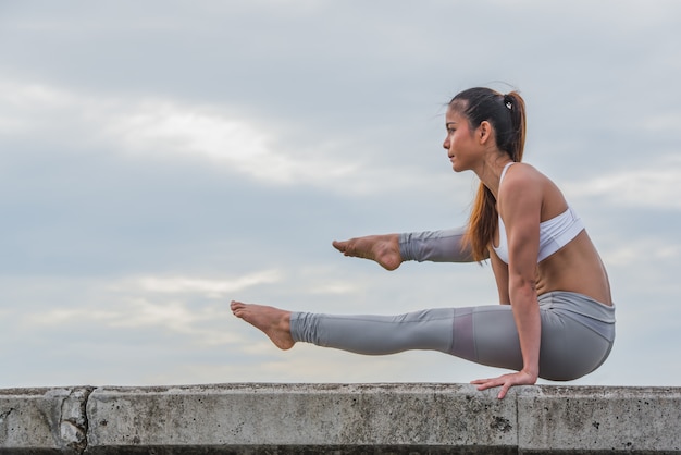 Asian woman in yoga pose on top of wall.