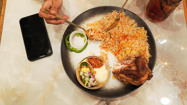 アジアの女性の手は,ケブリ米の皿に,スプーンとフォークで米を取っている. ナシ・ケブリ・タイピ