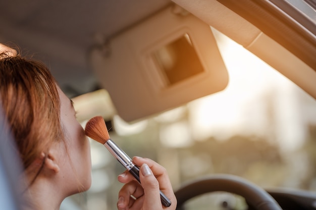 Asian women applying makeup in interior car  with looking mirror using brush make up