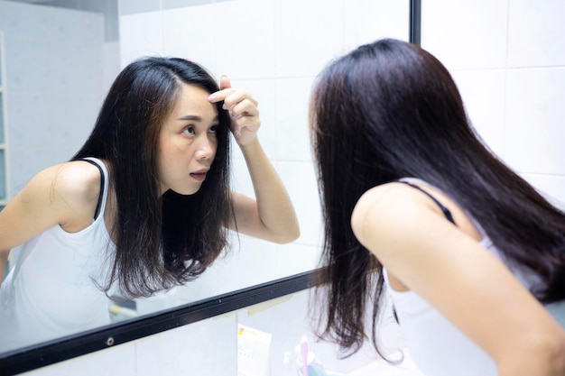 Asian women are exploring their faces due to acne looks in the mirror and crushes pimple Problem skin during menstruation Acne and hyperandrogenism due to hormonal disorders