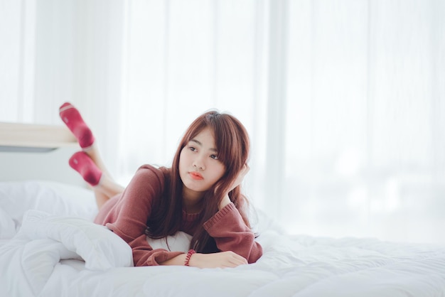 Asian women happily lie on the white bed in the house.