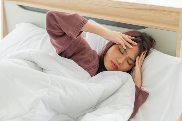 Азиатская женщина головная боль и спать на кровати
