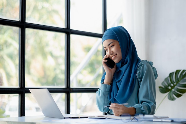 Donne asiatiche in hijab parlano al telefono amministrazione e operazioni delle donne che lavorano in modo intelligente di nuova generazione il concetto di gestione spinge l'azienda di donne leader a crescere