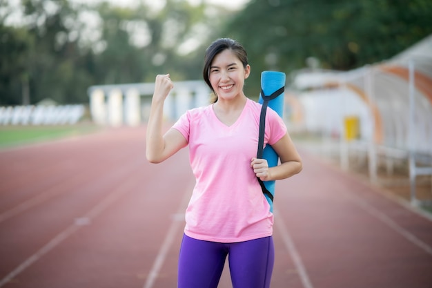 Asian women holding yoga mats are going to do yoga at the park to stay healthy and have good shape.