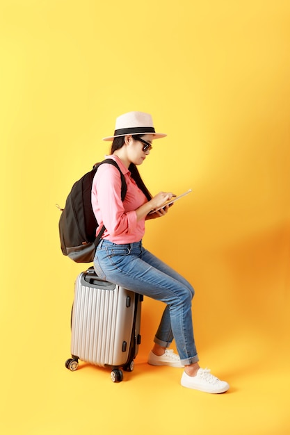 Asian women long hair wear Straw hat and sunglasses siting on travel bag in hand holding and use tablet