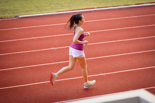 スタジアムトラックで晴れた朝に走っている中年のアジアの女性