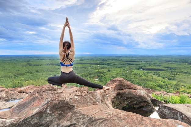 Asian women play it yoga on the mountain rock cliff.