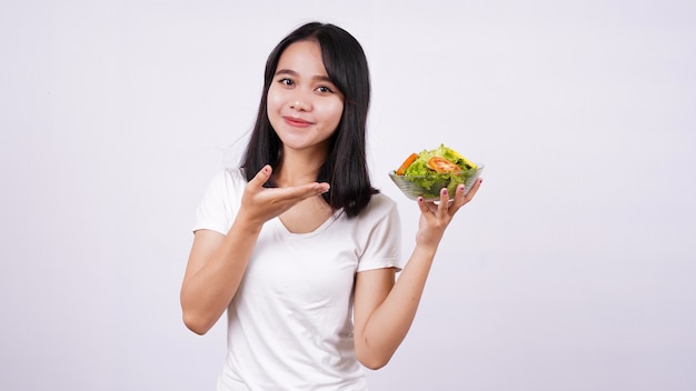 Asian women pointing finger at a bowl of fresh mixed vegetables salad with isolated white surface