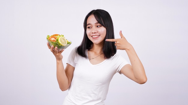 Asian women pointing finger at a bowl of fresh mixed vegetables salad with isolated white surface