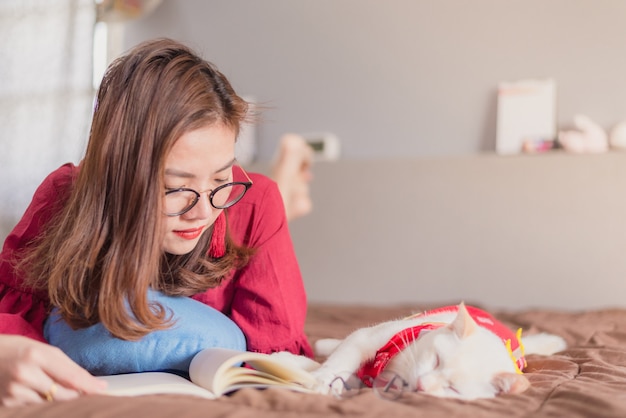 アジアの女性が自宅の猫と一緒にベッドで読書