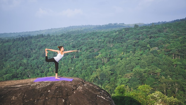 Foto le donne asiatiche si rilassano durante le vacanze. gioca se lo yoga. sulla falesia di moutain. natura delle foreste di montagna in thailandia. yoga di pratica della giovane donna nella felicità femminile della natura. esercizio di yoga