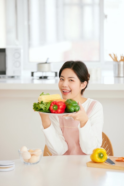 アジアの女性は新鮮な果物の野菜と一緒に台所のテーブルでリラックス