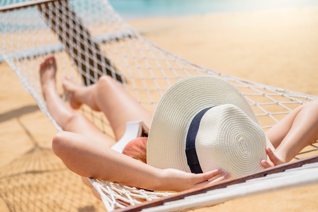 アジアの女性がビーチでハンモックの夏休みにリラックス