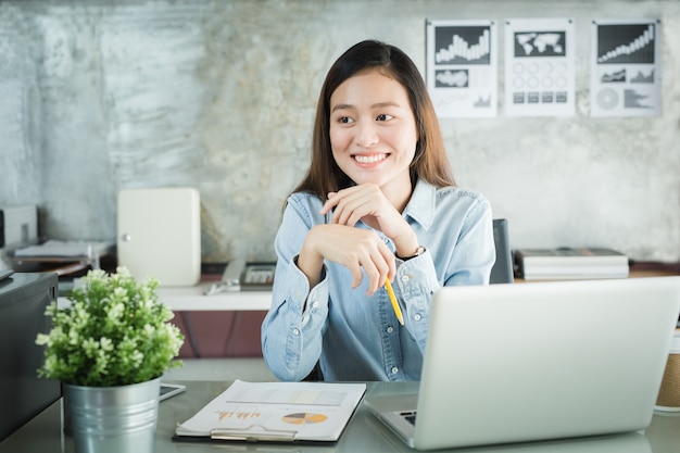 모바일 사무실 개념을 작업하는 동안 웃는 아시아 여성 앉아