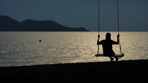 Foto donne asiatiche che si siedono nelle oscillazioni alla spiaggia durante il tramonto