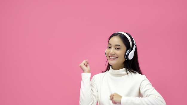 Asian women smiling and listening to the music with headphones on a pink studio background