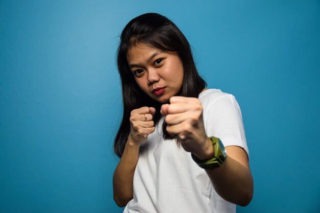 Asian women using white Tshirt with blue isolated background Punching fist to fight Fight gesture