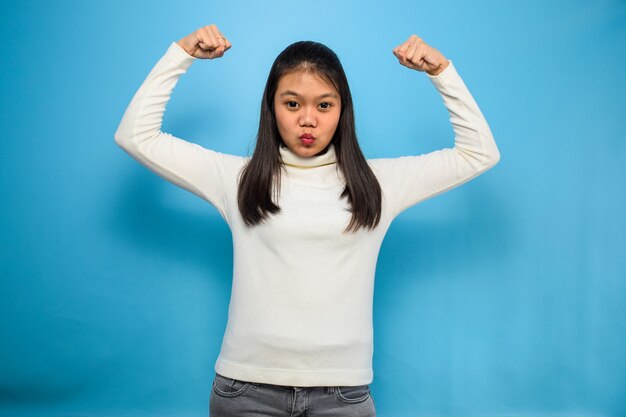 Asian women using white Tshirt with blue isolated background raises arms and shows biceps