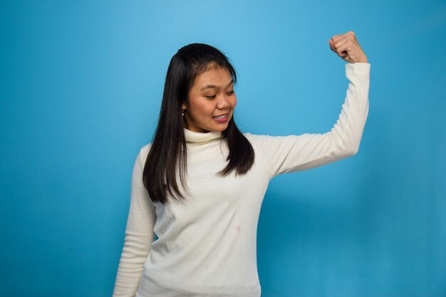 Photo asian women using white tshirt with blue isolated background raises arms and shows biceps