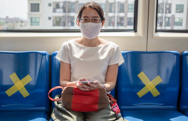 Asian women wear medical face mask, sitting on metro distance for one seat from other people