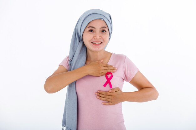 A asian women wearing headscarf disease with pink ribbon hand checking lumps on her breast for signs of breast mammary cancer isolated on white blank copy space studio background,medicine concept