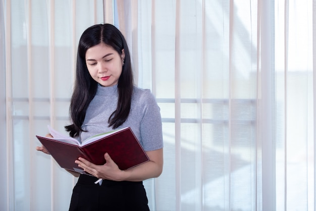 Donne asiatiche che indossano le maschere mediche che leggono un libro nella sua casa