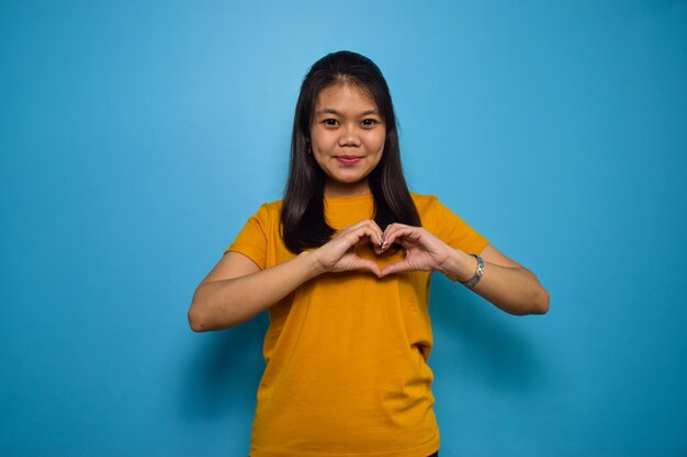 Asian women with blue isolated background shapes heart with both hands love gesture