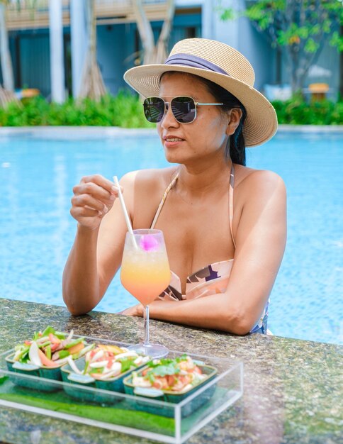 Asian women with hat and cocktail in hand relaxing in swimming
pool banner holiday vacation concept