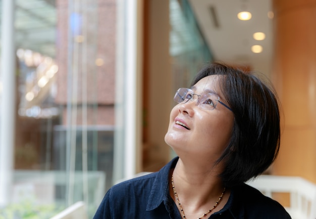 Photo asian women with short hair, short sleeve dress blue glasses sitting by the window glass.