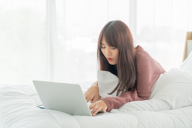 Donne asiatiche che lavorano con il computer portatile sul letto a casa