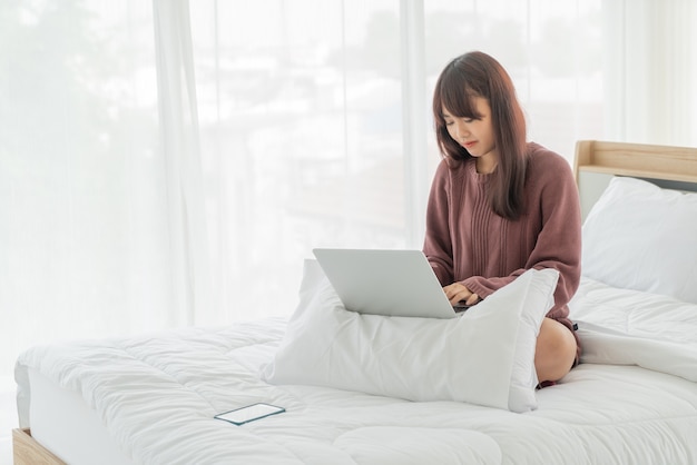 Donne asiatiche che lavorano con il computer portatile sul letto a casa