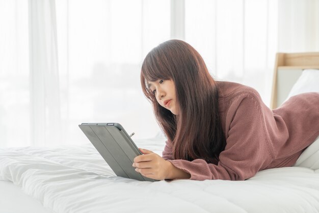 ベッドの上のタブレットを使用してアジアの女性