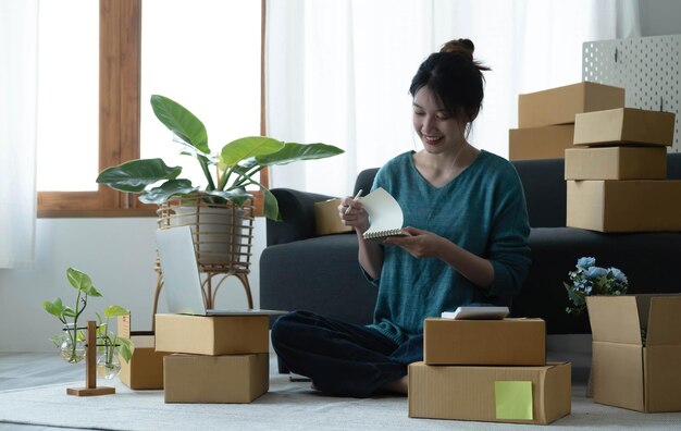 Le donne asiatiche scrivono una nota di ordini di merci con una faccia sorridente nel concetto di attività di e-commerce per piccole e medie imprese