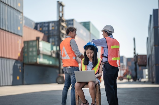 Asian worker girl working on laptop and sitting at background of containers cargo area