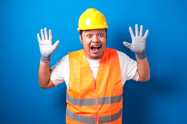 Asian worker wearing a helmet looks shocked hearing the news while closing his mouth with his hands 