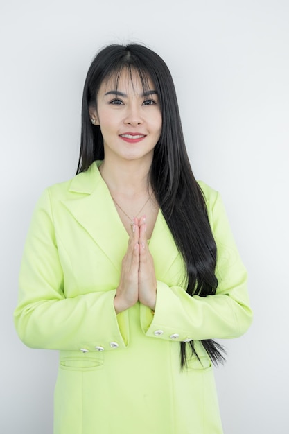 Asian working Thai business woman wearing green pastel suit made hello gesturing Sawasdee and smiling Thai culture friendly greeting Sawasdee symbol from Thailand greeting culture identity