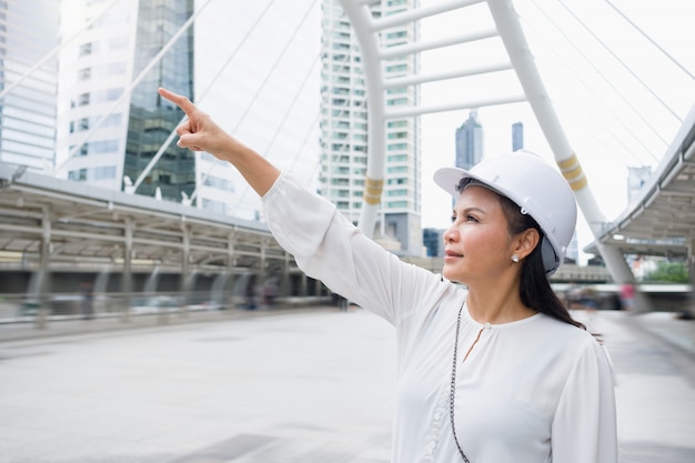 La donna lavoratrice asiatica che indossa un casco sta stando e indicando in avanti.