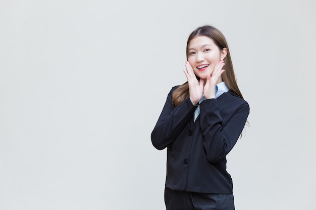 La donna lavoratrice asiatica che ha i capelli lunghi indossa un abito formale nero con una camicia blu mentre sorride felicemente su sfondo bianco.