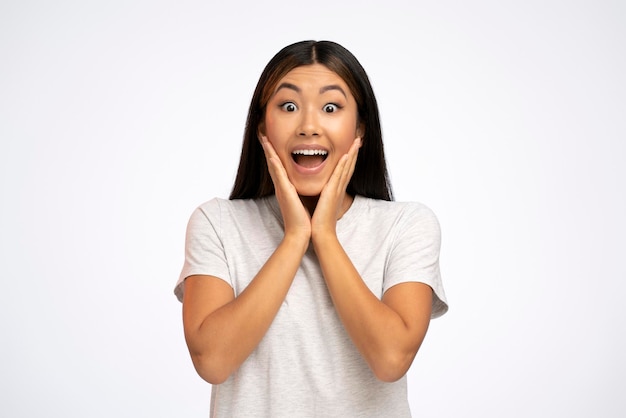 Asian young adult woman holding arms on her cheeks and shocked