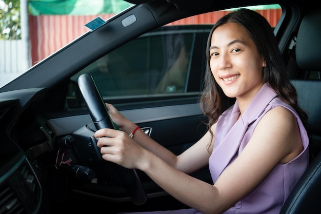 Asian young beautiful businesswoman sitting in her personal car\
in a driver seat and holding a steering wheel close up.