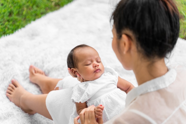 彼女の新生児を保持しているアジアの若い美しい母親は眠っていて、愛を感じています