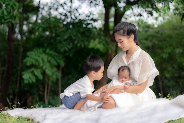 Asian young beautiful mother holding her newborn is sleeping and feel with love and touching gently then sitting on green grass in the park