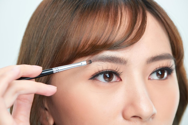 アジアの若い美しい女性が眉毛ナチュラルメイク美容顔に化粧品パウダー ブラシを適用します。