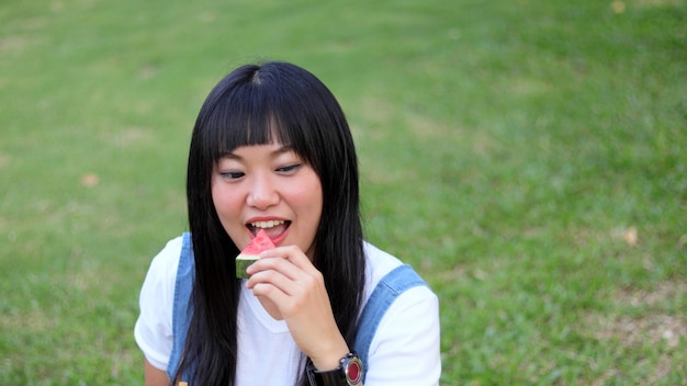 Фото Азиатская молодая красивая женщина ест свежий арбуз с улыбкой счастливым на открытом воздухе на прекрасный день.